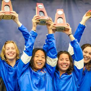 的 Pomona-Pitzer women’s swim and dive team smile and hold up the NCAA trophies above their heads.